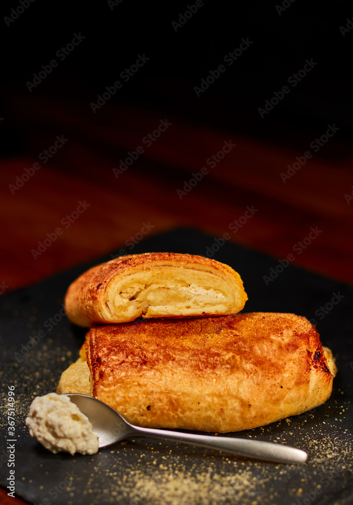 Freshly made rolled bun with fresh cheese on black stone cutting board, sprinkled with corn flour. Very shallow depth of field