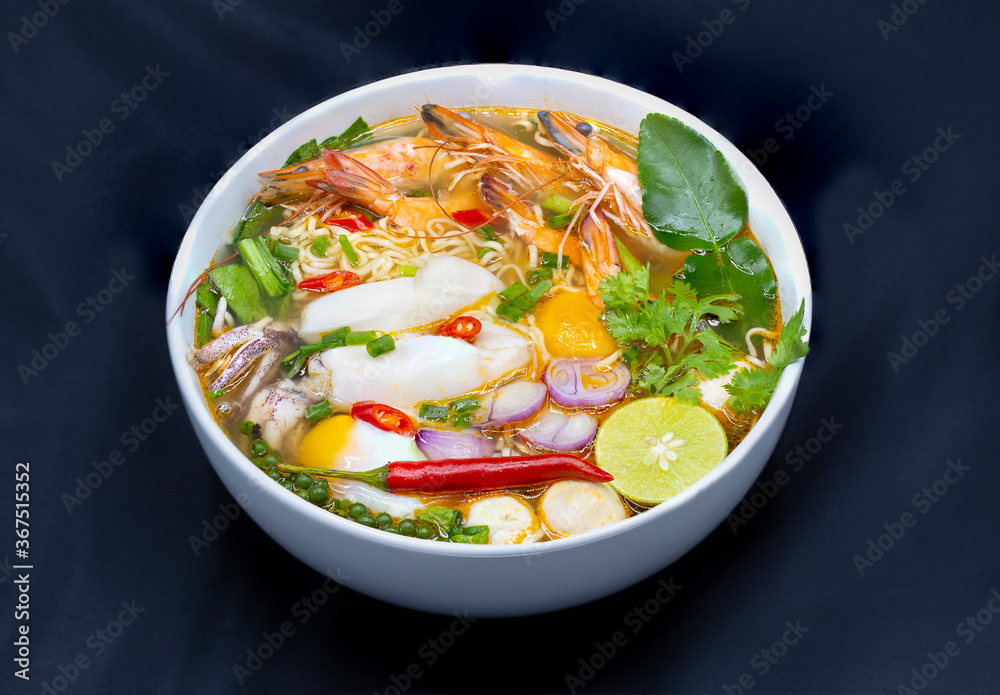 Tom Yum Kung, Thailand favorite spicy boiled food with ingredient are prawn, squid, fish, egg, meat ball and many spicy Thai herb, ready to serve in white bowl on dark background.
