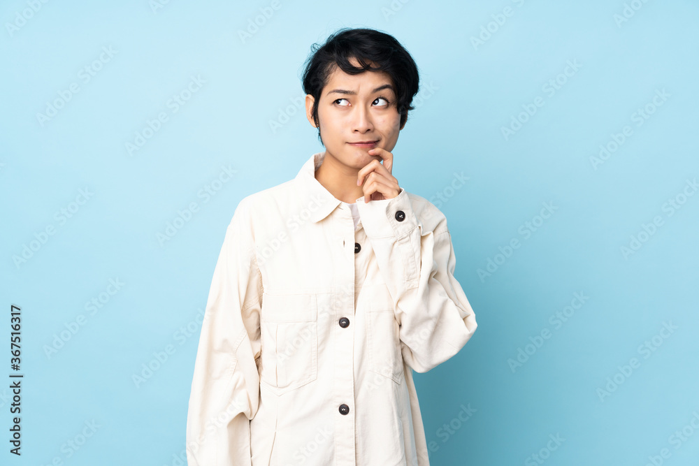 Young Vietnamese woman with short hair over isolated background having doubts and thinking Young Vietnamese woman with short hair over isolated background having doubts and thinking