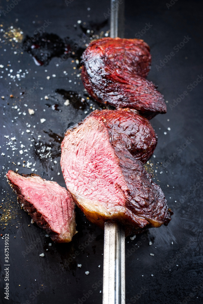 Barbecue dry aged wagyu Brazilian picanha from the sirloin cap of rump beef sliced and offered as close-up on a skewer on a rustic old board with copy space