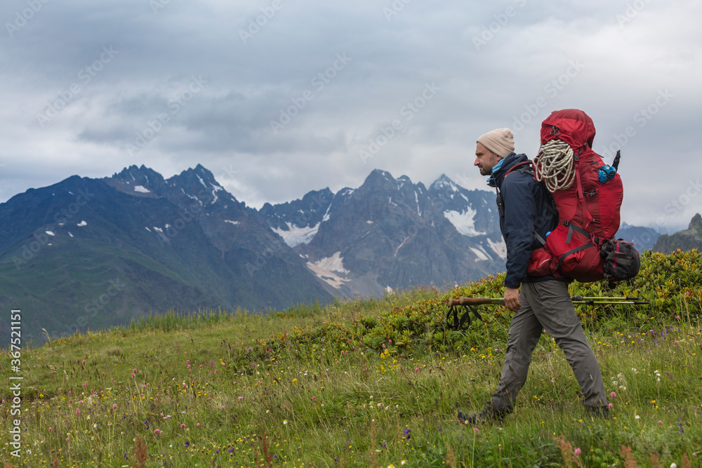 A hiker with hiking backpack in mountains. Tourist in Svaneti on a background of the main Caucasus ridge and snow-capped mountain peaks.