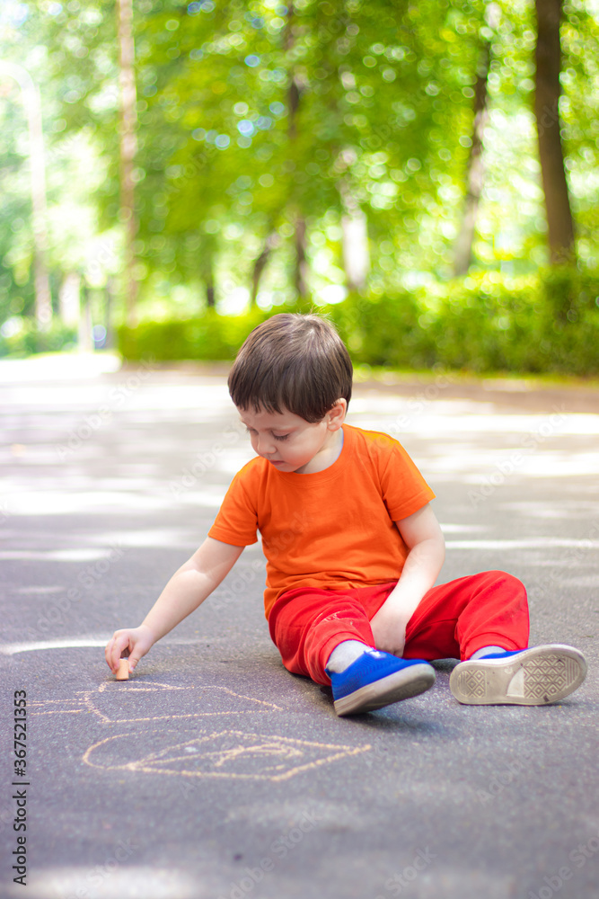 Fototapeta premium A boy draws with crayons on the asphalt . Painting. Summer. Summer games on the street. Children's entertainment and leisure. Chalk for asphalt .