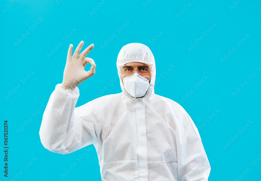 Doctor in protective medical suit showing ok sign isolated on blue background Doctor in protective medical suit showing ok sign isolated on blue background