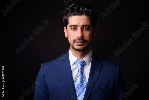 Young handsome bearded Persian businessman against black background