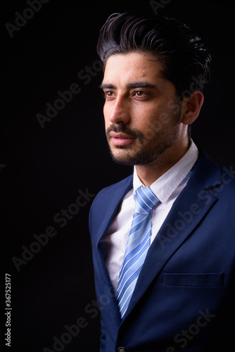 Young handsome bearded Persian businessman against black background