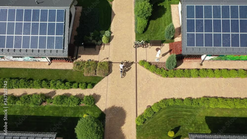A man and a boy ride a two-seater bike along the trail of an elite village with eco-friendly smart homes equipped with solar panels that generate electricity. Alternative energy and a healthy lifestyl