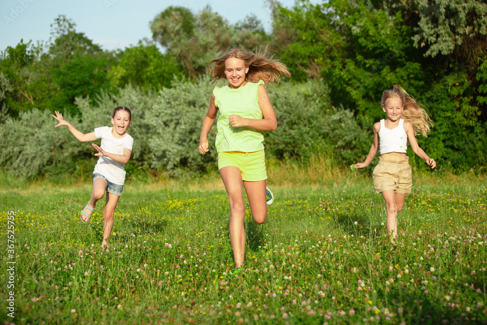 Kids, children running on meadow in summer's sunlight. Look happy, cheerful with sincere bright emotions. Cute caucasian boys and girls. Concept of childhood, happiness, movement, family and summer.