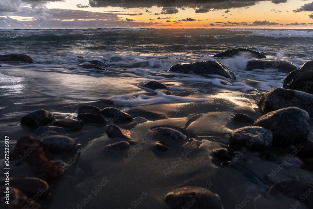 Obraz premium long exposure landscape, rocky ocean coastline with blurry waves in orange sunset light