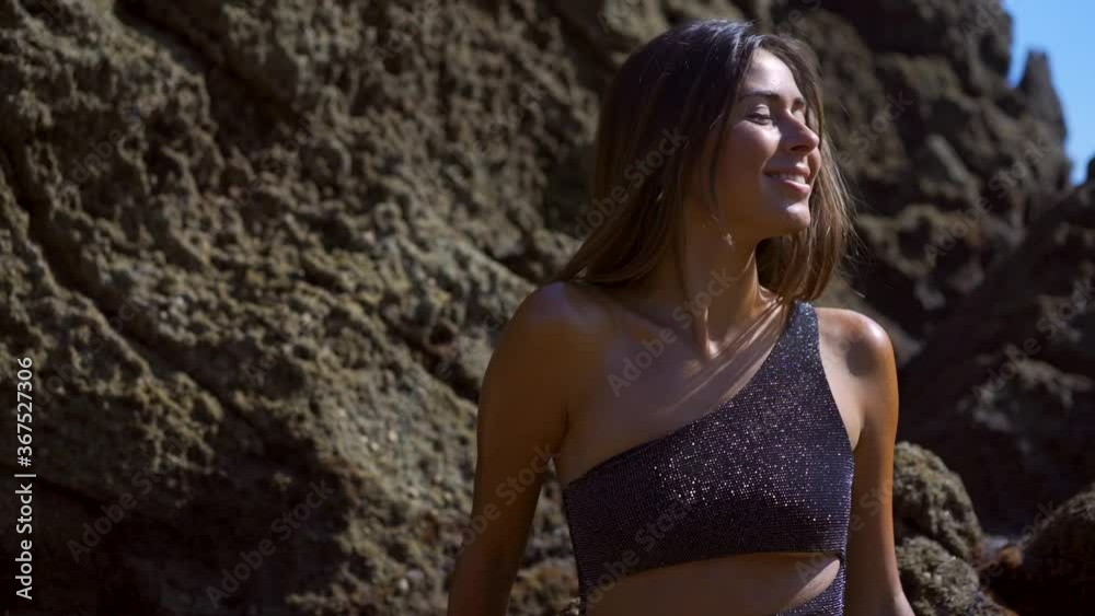 Perched of a pretty young caucasian brunette with black swimsuit in a cove on the Cantabrian coast enjoying the summer, summer lifestyle. Sitting by the sea water