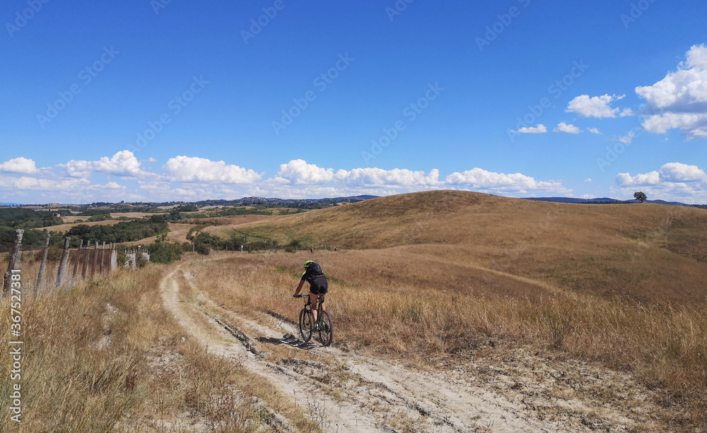 ciclista solitario in discesa tra i campi e il cielo azzurro della toscana