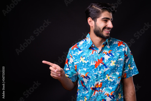 Young handsome bearded Persian tourist man ready for vacation against black background