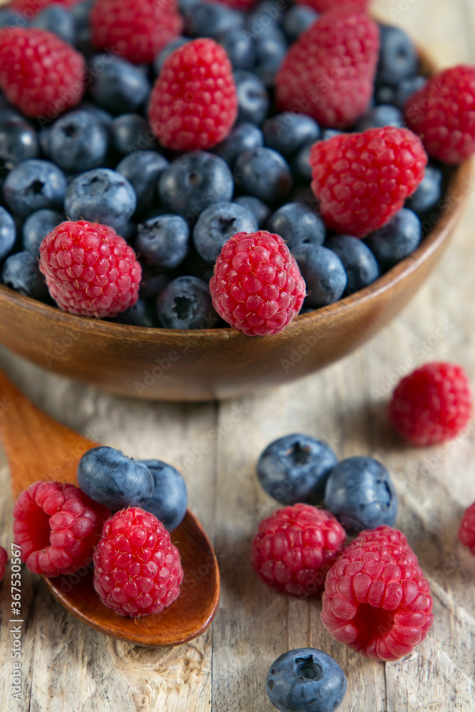 Blueberries and raspberries in a wooden bowl on a wooden table. Blueberries and raspberries in a wooden bowl on a wooden table.