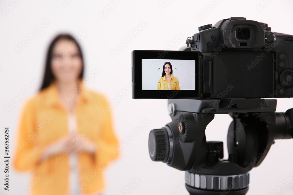 Young blogger recording video against white background, focus on camera screen