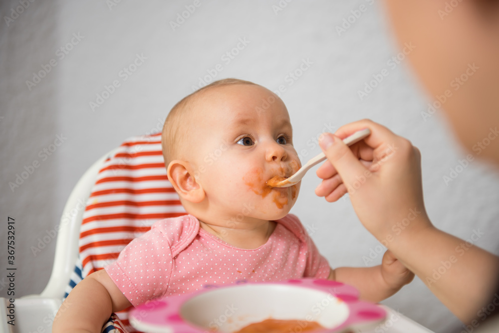 Mother feeding her baby girl with spoon in high chair Mother feeding her baby girl with spoon in high chair