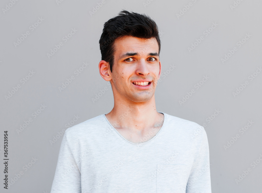 Indoor shot of puzzled and confused man showing teeth while looking at camera and standing over gray background. Husband forgot to throw garbage and now says sorry