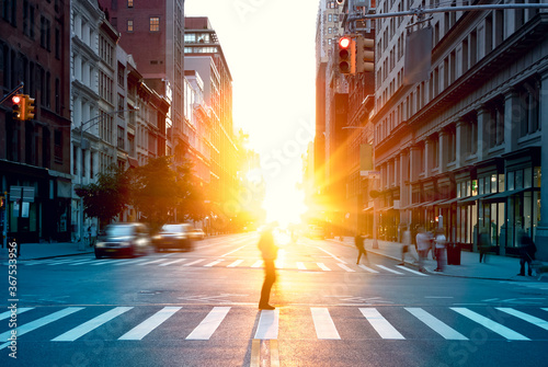 Blurred image of a man walking across the street in New York City with the bright light of sunset shining through the buildings