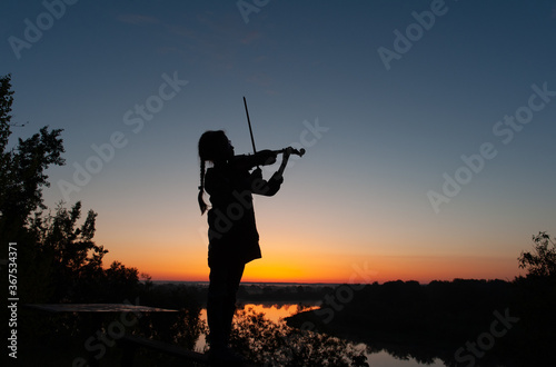 Silhouette of a teenage girl with a violin on a background of blue sky in natural light