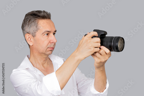 Portrait of handsome man in white shirt takes picture with camera. Isolated grey background