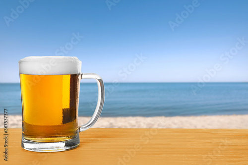 Cold beer on wooden desk against blurred sea. Space for text