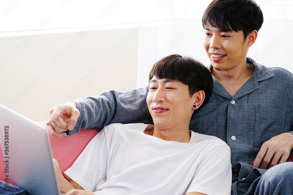 Young LGBT couple using laptop together on sofa Young LGBT couple using laptop together on sofa