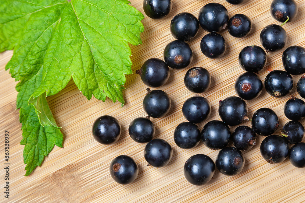 Fresh ripe black currants heap on wooden background. Natural organic berries with green leaves scattered on weathered wooden table, new berry harvest. Top view Fresh ripe black currants heap on wooden background. Natural organic berries with green leaves scattered on weathered wooden table, new berry harvest. Top view