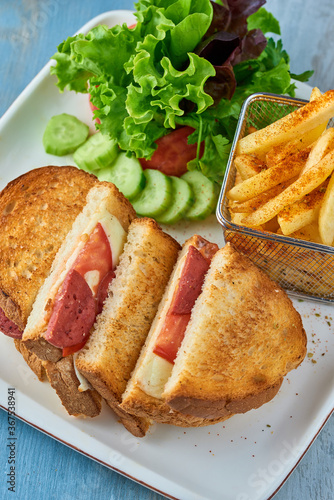 Grilled and pressed toast with turkish sausage, cheese, tomato and lettuce served on white plate.