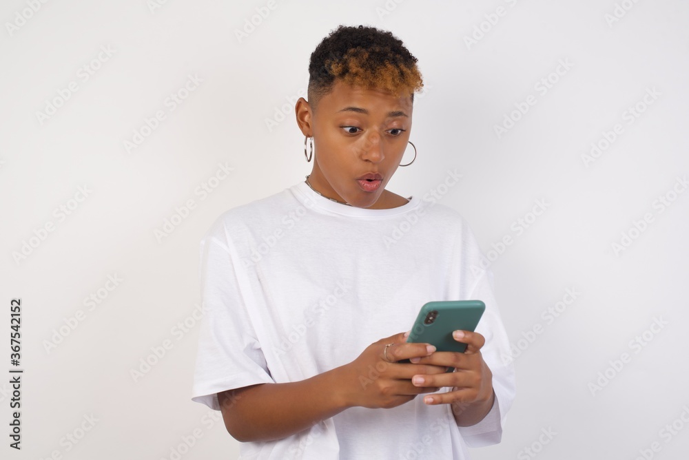 Horizontal shot of pretty young female isolated over pink background, looks with bugged eyes, holds modern smart phone, receives unexpected message from friend, reads reminder. Horizontal shot of pretty young female isolated over pink background, looks with bugged eyes, holds modern smart phone, receives unexpected message from friend, reads reminder.
