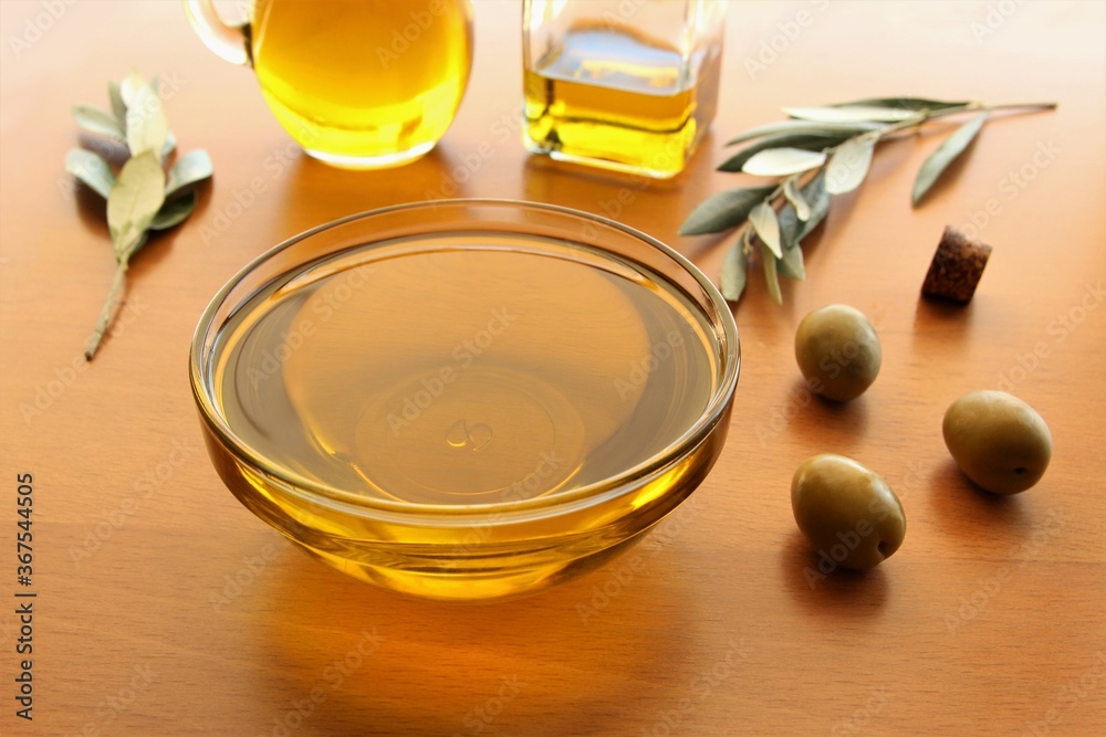 Olive oil bowl and green olives with blurred of olive branches, olive jar, olive bottle in the back. photo Olive oil bowl and green olives with blurred of olive branches, olive jar, olive bottle in the back. photo