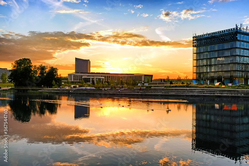 summer sunset in modern city landmark against city skyline background. Street wide view of duck pond and people at Skolkovo business district in Moscow city Russia. Office tower and setting sun