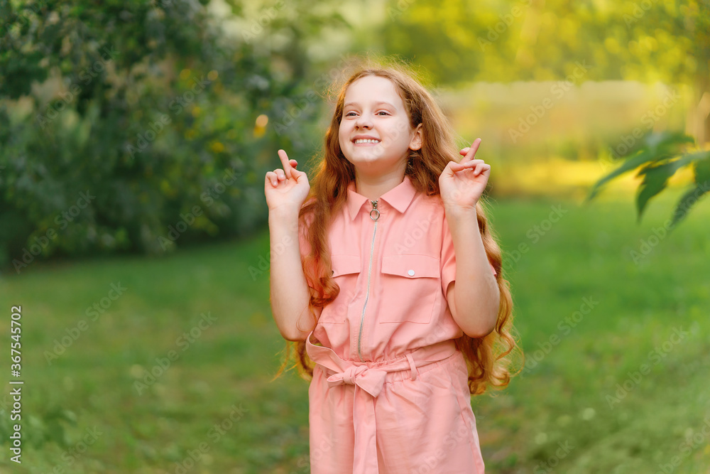 Little redhead girl raises fingers crossed and makes desirable wish outdoors. Little redhead girl raises fingers crossed and makes desirable wish outdoors.
