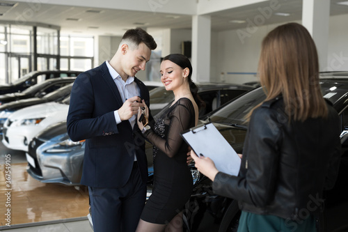 A couple of men and women are happy to buy a new car in a car dealership with the seller.