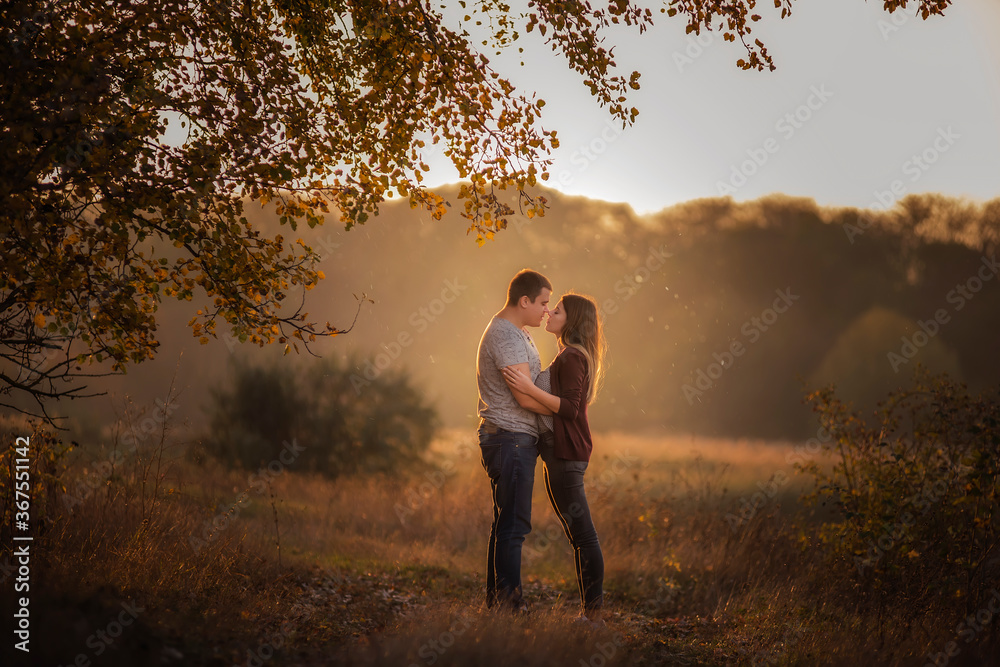 A young man and a girl are walking in the autumn forest. Happy lovers hold hands, hug each other, kiss, spend time together. Traveling during the cold season, on weekend days. Couple in love forever