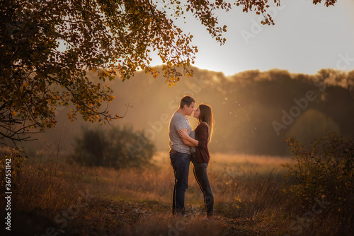 A young man and a girl are walking in the autumn forest. Happy lovers hold hands  hug each other  kiss  spend time together. Traveling during the cold season  on weekend days. Couple in love forever