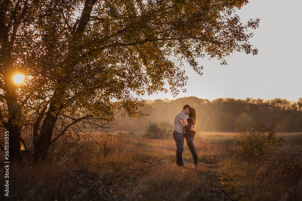 A young man and a girl are walking in the autumn forest. Happy lovers hold hands, hug each other, kiss, spend time together. Traveling during the cold season, on weekend days. Couple in love forever