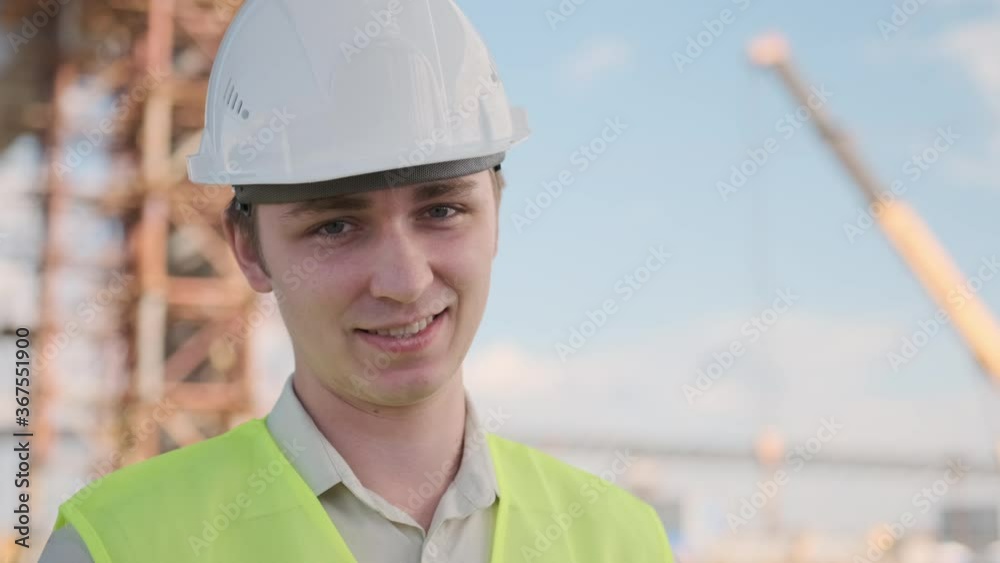 Portrait of young smiling architect in white helmet looking at camera on background of object under construction. Portrait of young smiling architect in white helmet looking at camera on background of object under construction.