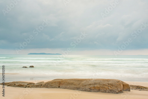 Fototapeta Naklejka Na Ścianę i Meble -  Tranquil scene of a beach at the sea with an island in the background and rocks in the foreground