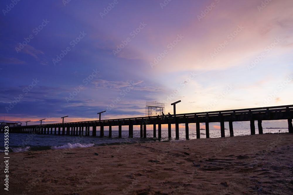 Old pier, bridge with relaxing silhouette of people on bridge and beach in the colorful backdrop in the evening time