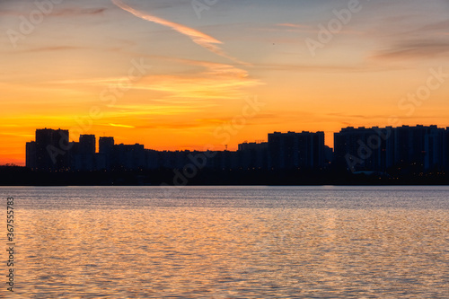 Silhouette of urban buildings against the backdrop of the sunset reflected in the water