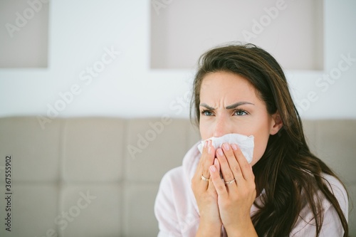 Female covering her face while sneezing sitting on the bed