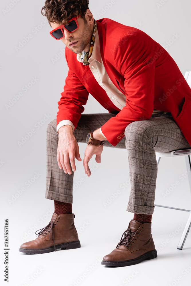Trendy, handsome man leaning forward and  posing while sitting on chair on grey