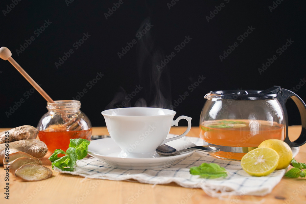 Cup of hot ginger tea with honey, lemon and mint with steam from cup on wooden table over black background. the concept of natural medicine.