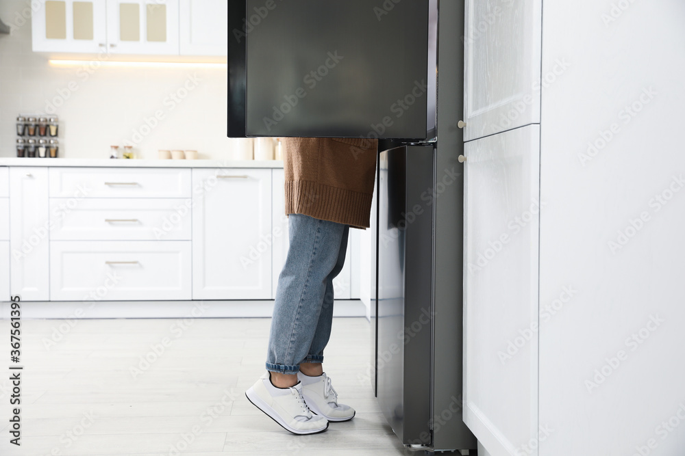Young woman looking into refrigerator in kitchen Young woman looking into refrigerator in kitchen