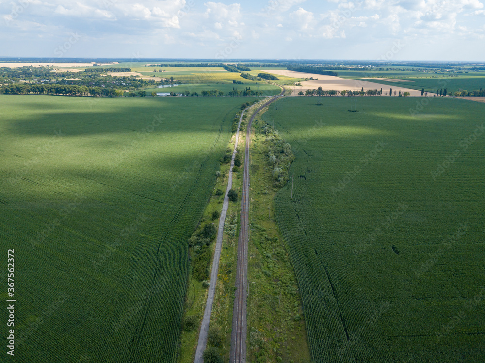 Railroad through a green corn field in Ukraine. Aerial drone view.