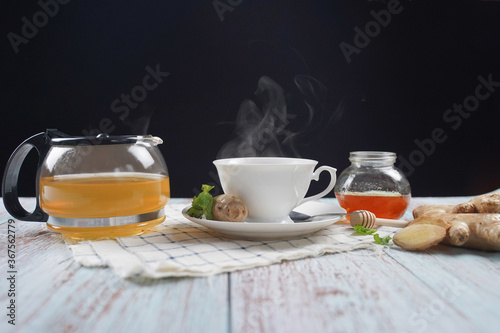 Cup of hot ginger tea with honey and mint with steam from cup on wooden table over black background. the concept of natural medicine.