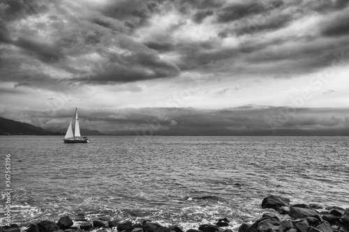 Картината върху платно Greyscale shot of a sailboat in the sea with a cloudy sky over it