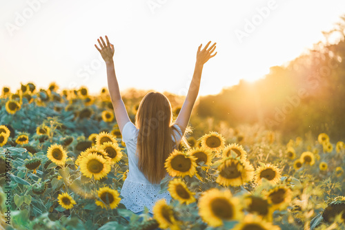Young beautiful woman smiling and having fun in a sunflower field on a beautiful summer day with arms raised up.