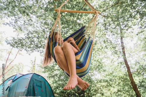 A young woman relaxing in a hammock. Girl resting in the woods  camping in a hammock. Healthy lifestyle in the forest.