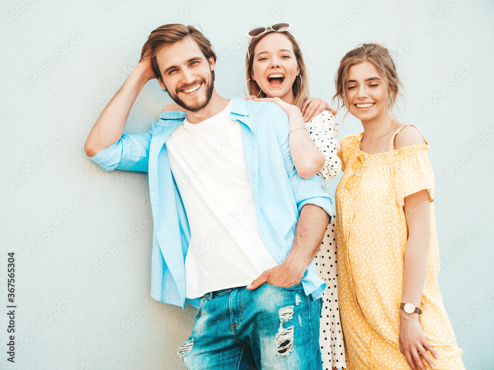 Group of young three stylish friends posing in the street. Fashion man and two cute girls dressed in casual summer clothes. Smiling models having fun near wall.Cheerful women and guy outdoors Group of young three stylish friends posing in the street. Fashion man and two cute girls dressed in casual summer clothes. Smiling models having fun near wall.Cheerful women and guy outdoors
