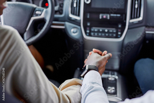 lovely black couple holds each other's hand while sitting inside of car. in dealership