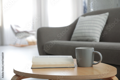 Book and cup of coffee on table near sofa. Interior design